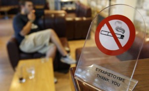 A man smokes a cigarette behind a smoking ban sign in a cafe in Chalandri suburb, north of Athens
